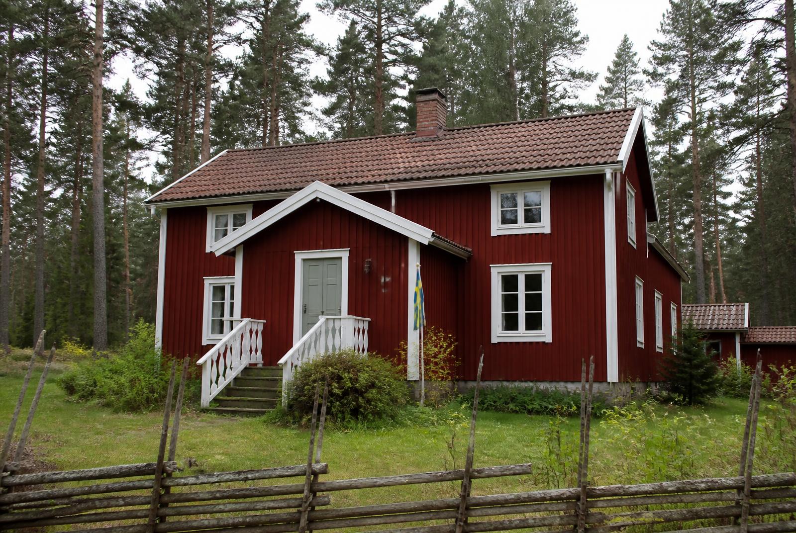 Typisk svensk rødmalet træhus med hvide vinduer i skovomgivelser